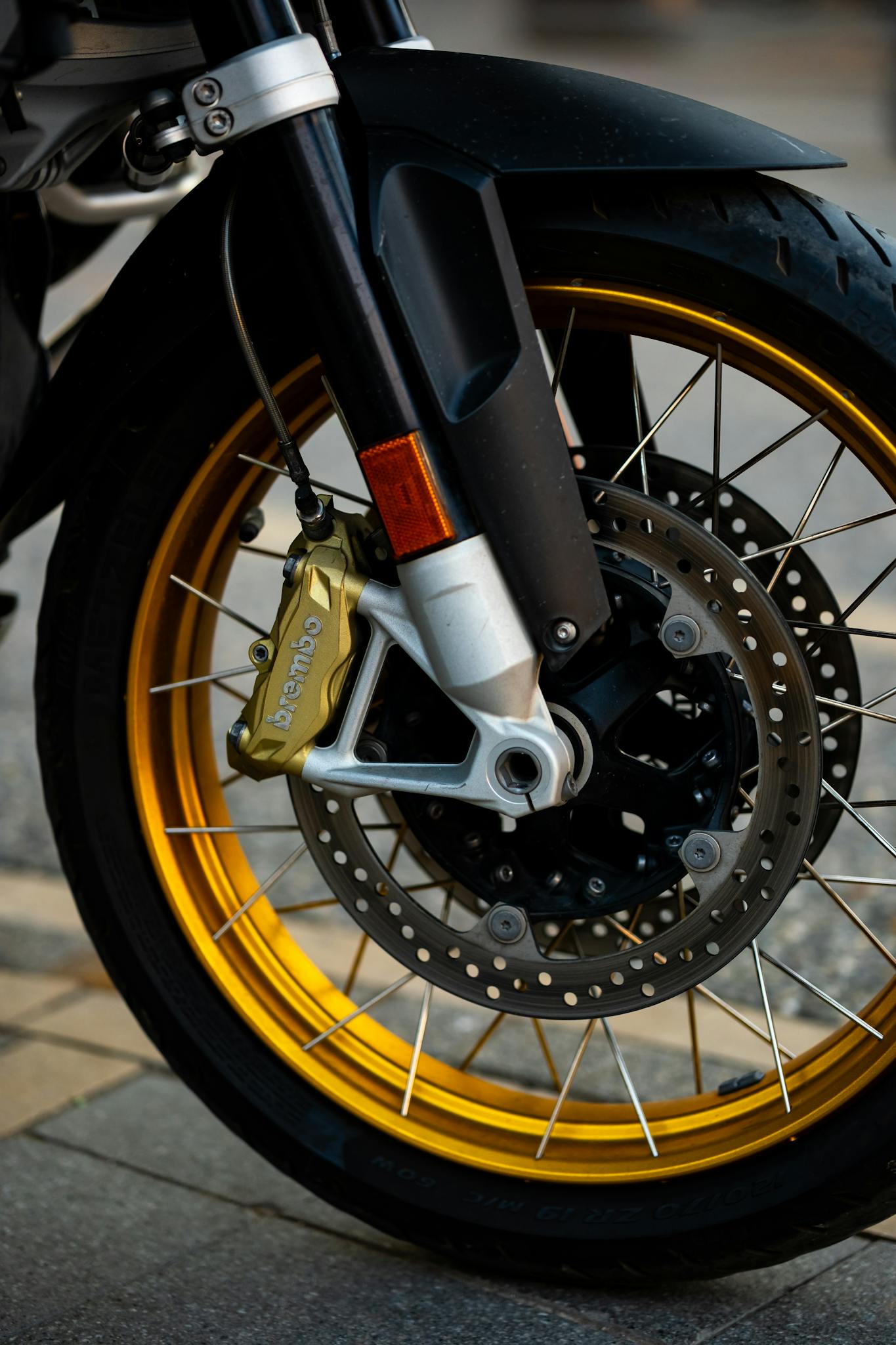 Detailed view of a motorcycle front wheel with golden rims and Brembo brake calipers, captured outdoors.