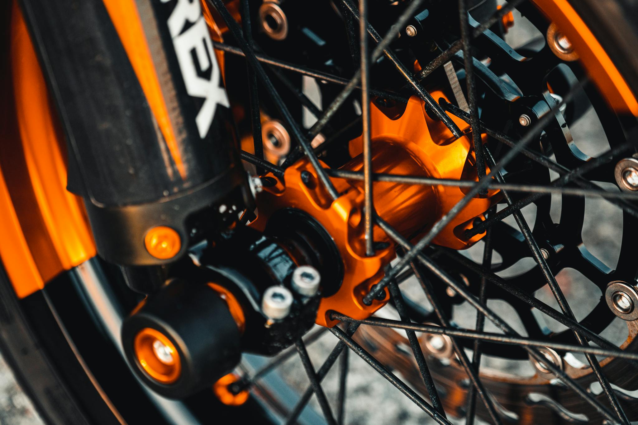 Detailed view of a motorcycle wheel highlighting the spokes, metal structure, and vibrant orange accents.