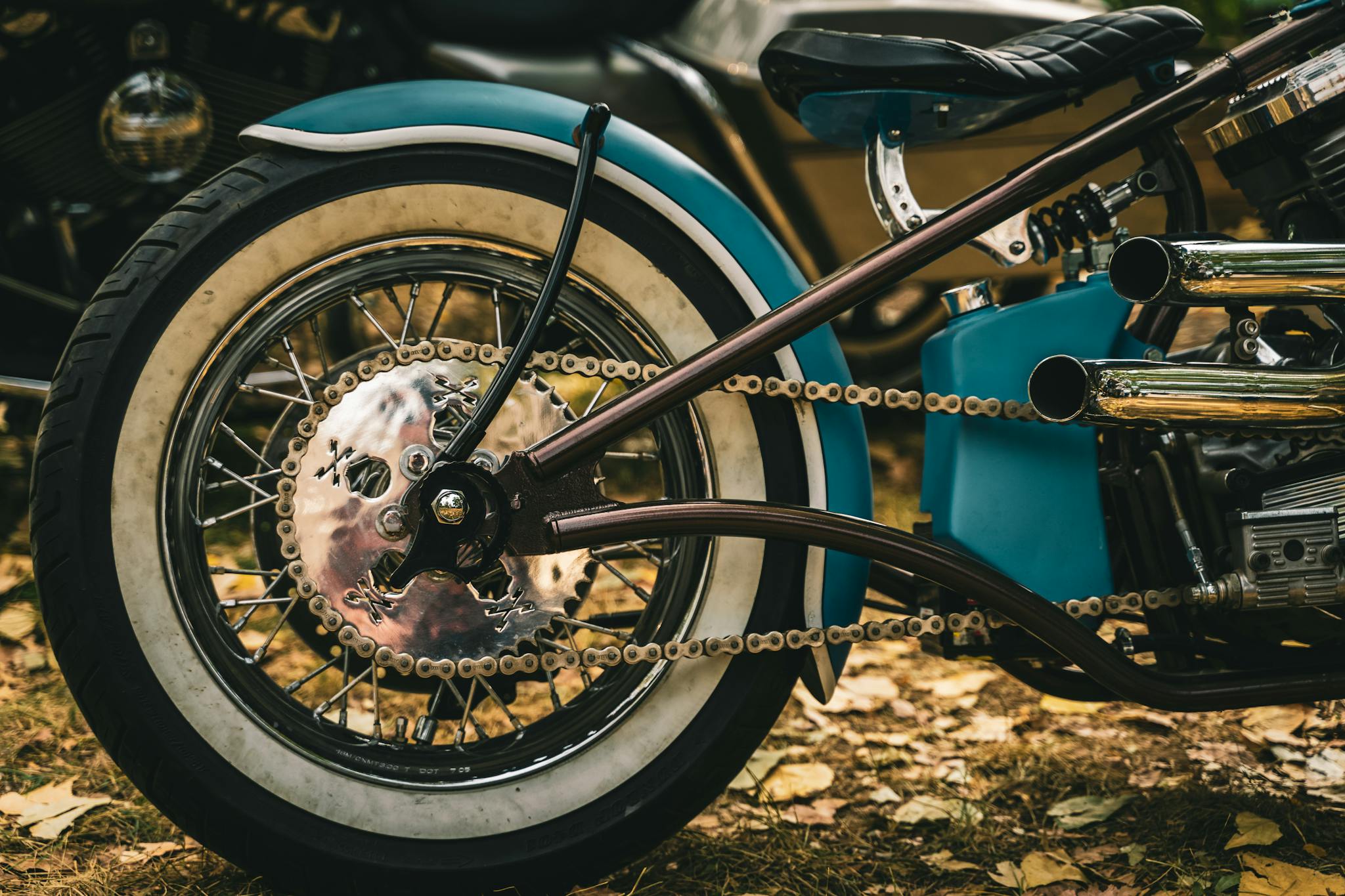 Detailed view of a vintage motorcycle's rear wheel with chrome accents in outdoor setting.