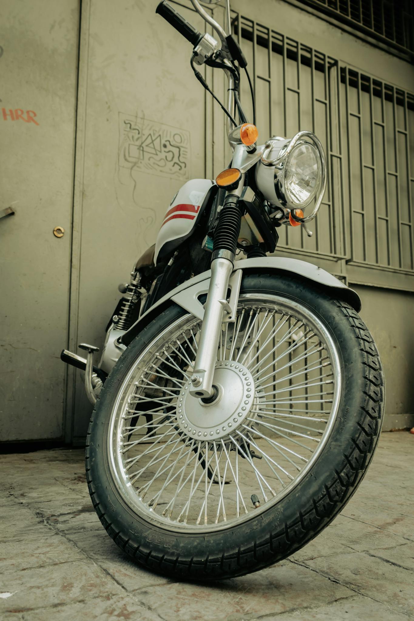Low angle shot of a vintage motorcycle parked against a graffitied wall.